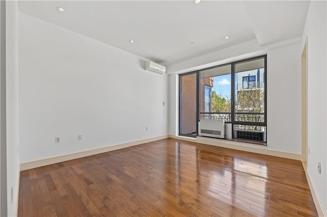empty room with wood-type flooring, a wall unit AC, baseboards, and recessed lighting