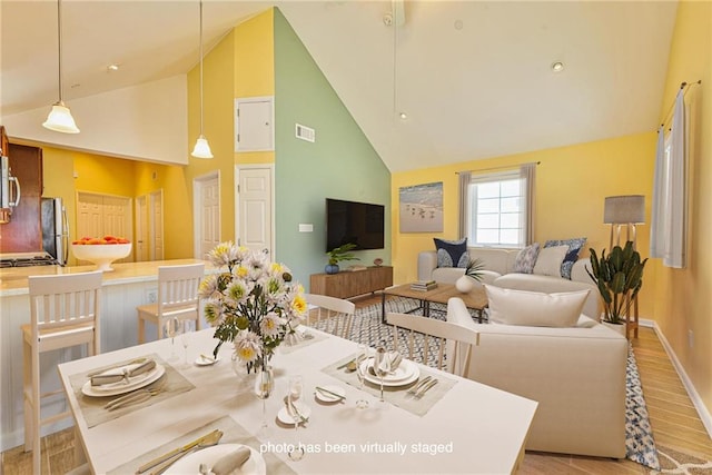 dining space featuring high vaulted ceiling, light wood-style floors, and baseboards