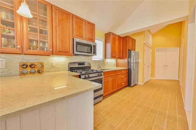 kitchen featuring stainless steel appliances, lofted ceiling, decorative backsplash, a sink, and brown cabinets