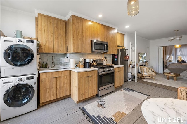 kitchen featuring stainless steel appliances, stacked washing machine and dryer, a sink, light countertops, and decorative backsplash
