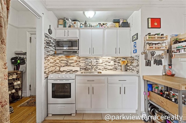 kitchen featuring a sink, stainless steel microwave, white gas range, light countertops, and white cabinets