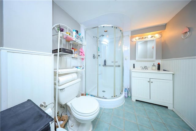 full bathroom featuring a wainscoted wall, a shower stall, toilet, vanity, and tile patterned floors