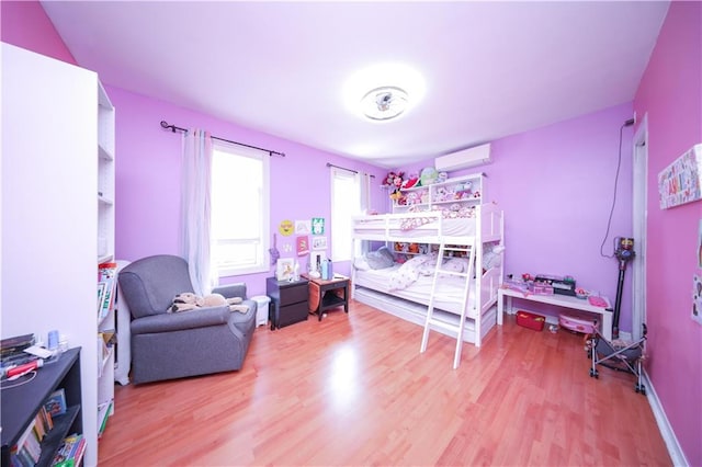 bedroom featuring a wall unit AC, wood finished floors, and baseboards