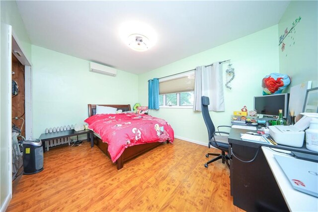bedroom featuring a wall mounted AC, light wood-type flooring, an office area, and baseboards