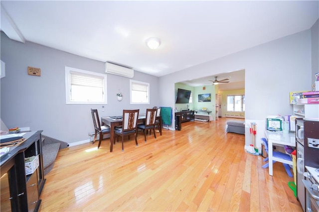 dining space featuring an AC wall unit, light wood-style flooring, and a ceiling fan