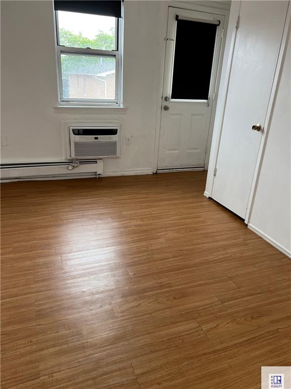 spare room with a baseboard radiator, wood finished floors, an AC wall unit, and baseboards