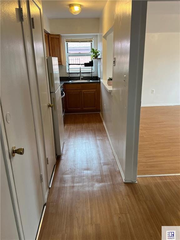 hall with wood finished floors, a sink, and baseboards