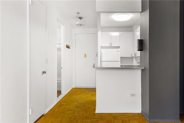 kitchen featuring freestanding refrigerator, white cabinetry, and a peninsula
