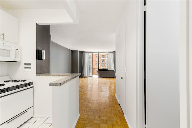 kitchen featuring white appliances, a peninsula, baseboards, light countertops, and white cabinetry