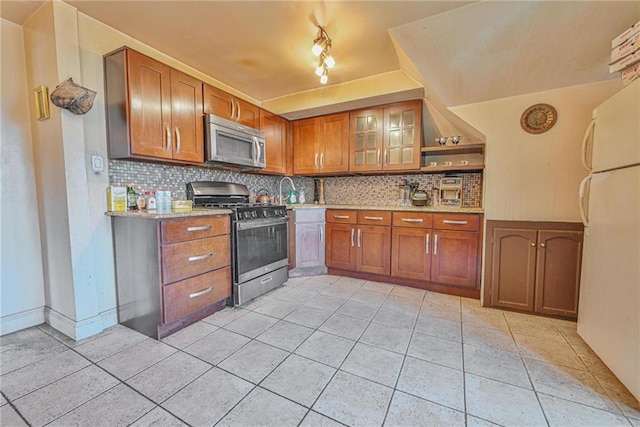 1401 74th St, Brooklyn, NY 11228 - kitchen featuring appliances with stainless steel finishes, light tile patterned floors, brown cabinets, backsplash, and glass insert cabinets