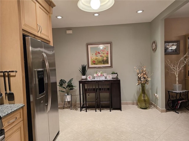kitchen with stainless steel refrigerator with ice dispenser, light stone counters, light tile patterned floors, light brown cabinetry, and recessed lighting