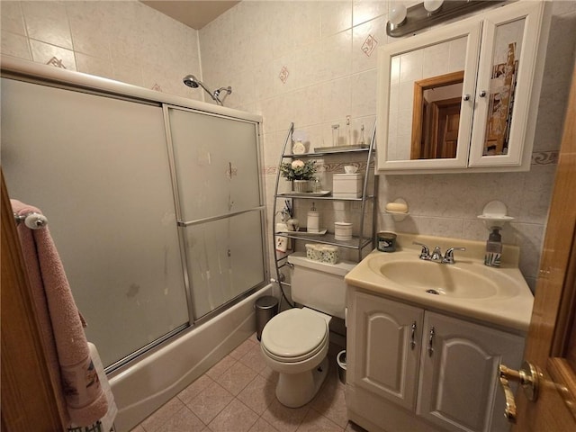 full bathroom with tile walls, bath / shower combo with glass door, toilet, vanity, and tile patterned flooring