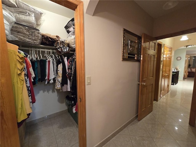 hall featuring arched walkways, tile patterned floors, and baseboards