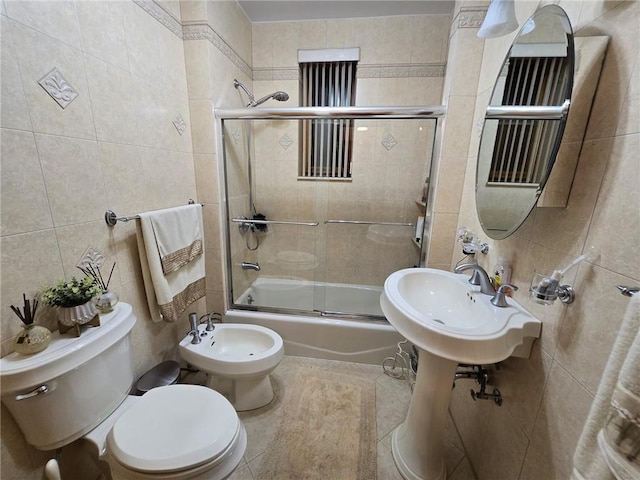 bathroom with tile walls, toilet, a bidet, bath / shower combo with glass door, and tile patterned floors