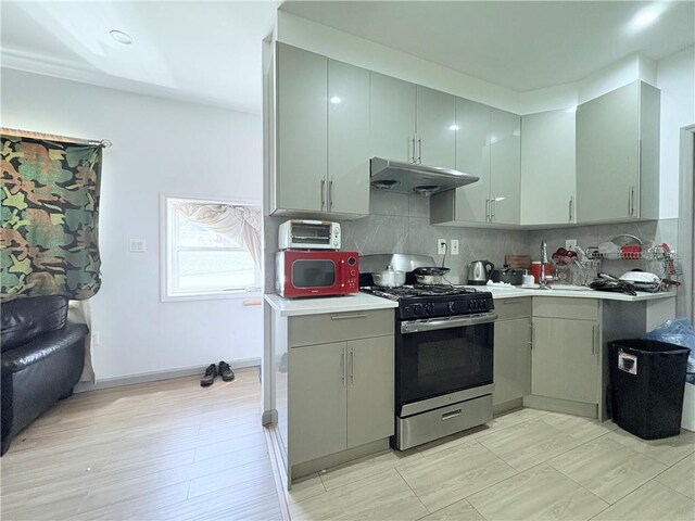 2349 W 12th St, Brooklyn, NY 11223 - kitchen with gas range, under cabinet range hood, decorative backsplash, light countertops, and gray cabinetry