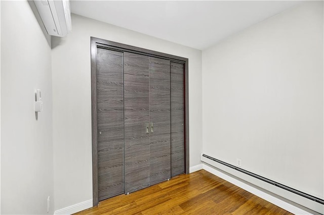 unfurnished bedroom with baseboard heating, wood finished floors, and baseboards