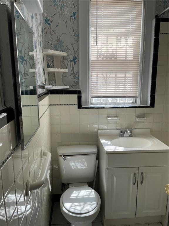 bathroom featuring tile walls, wallpapered walls, toilet, and vanity