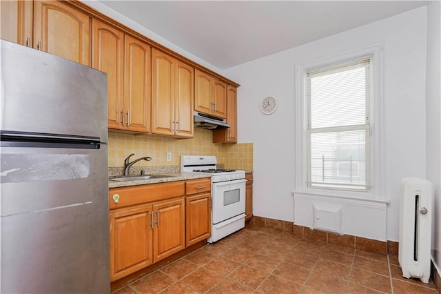 kitchen featuring gas range gas stove, freestanding refrigerator, under cabinet range hood, a sink, and decorative backsplash