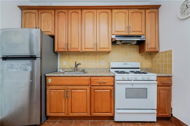 kitchen with freestanding refrigerator, white range with gas cooktop, a sink, under cabinet range hood, and tasteful backsplash