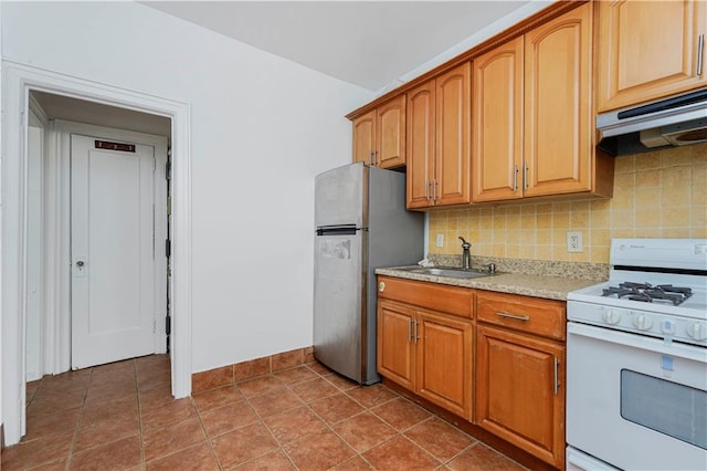 kitchen featuring white gas range oven, a sink, freestanding refrigerator, tasteful backsplash, and under cabinet range hood
