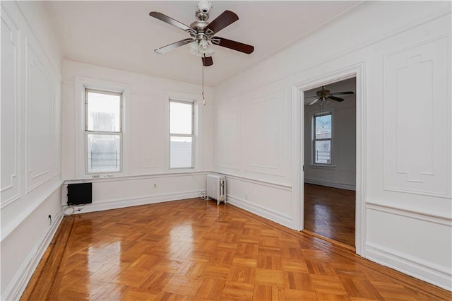 unfurnished room with radiator, a ceiling fan, and a decorative wall