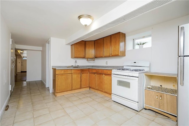 kitchen with white gas range, freestanding refrigerator, a sink, light countertops, and brown cabinets
