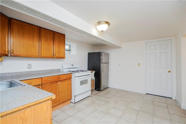 kitchen featuring white range with gas cooktop, freestanding refrigerator, light countertops, and brown cabinets