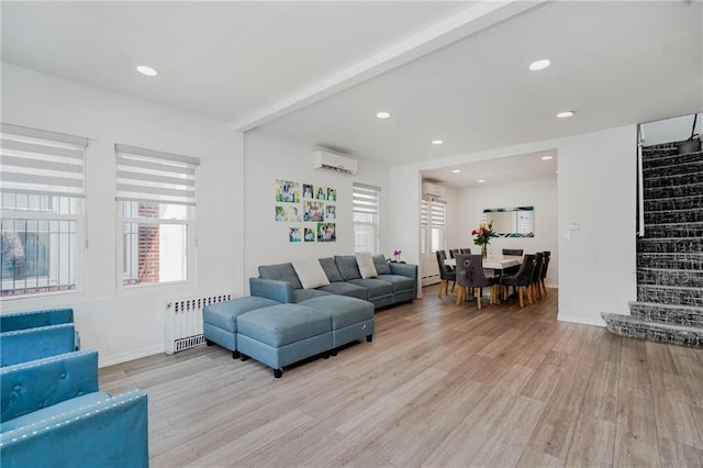 living area with radiator, a wall unit AC, stairway, light wood-style floors, and baseboards