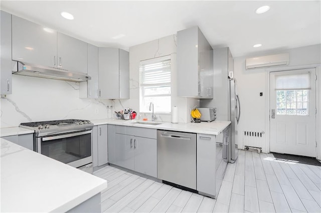kitchen with appliances with stainless steel finishes, gray cabinetry, under cabinet range hood, a wall mounted AC, and a sink