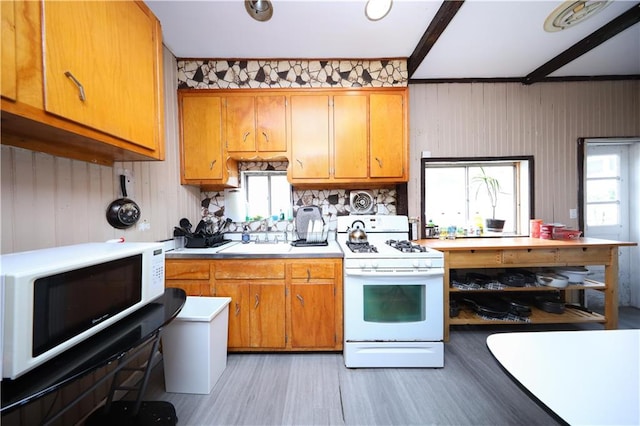 kitchen with white appliances, light countertops, brown cabinetry, healthy amount of natural light, and wood walls