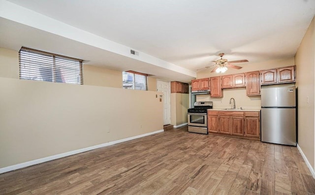 kitchen with appliances with stainless steel finishes, light wood-style floors, baseboards, light countertops, and under cabinet range hood