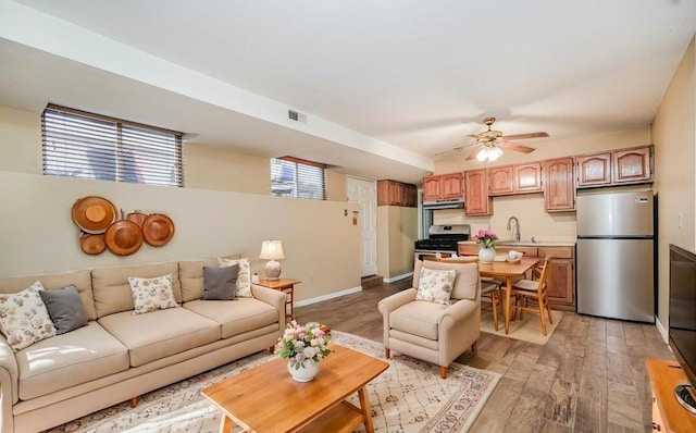 living area featuring light wood-style flooring, a ceiling fan, and baseboards