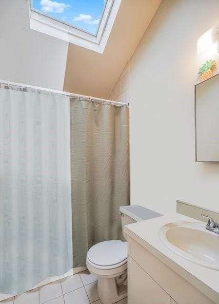 bathroom with a skylight, tile patterned floors, vanity, toilet, and lofted ceiling
