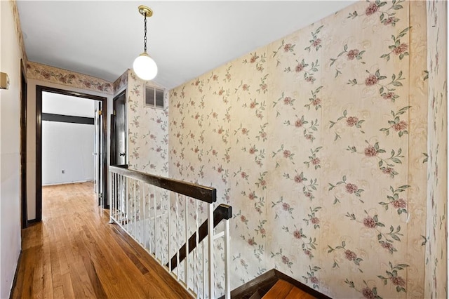 hall with an upstairs landing, hardwood / wood-style floors, wallpapered walls, and baseboards