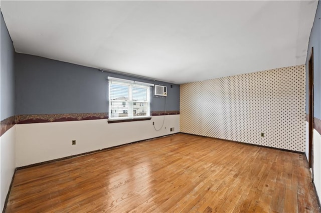 empty room featuring wallpapered walls, an accent wall, light wood finished floors, and baseboards