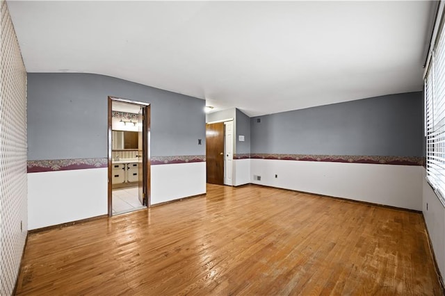 empty room with wood finished floors, lofted ceiling, and wainscoting