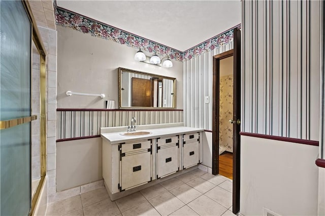 bathroom with wallpapered walls, tile patterned flooring, a shower with shower door, and vanity