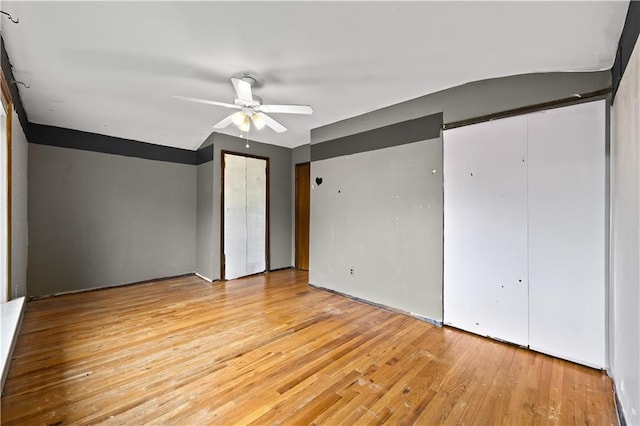 unfurnished bedroom with two closets, light wood-style flooring, and ceiling fan