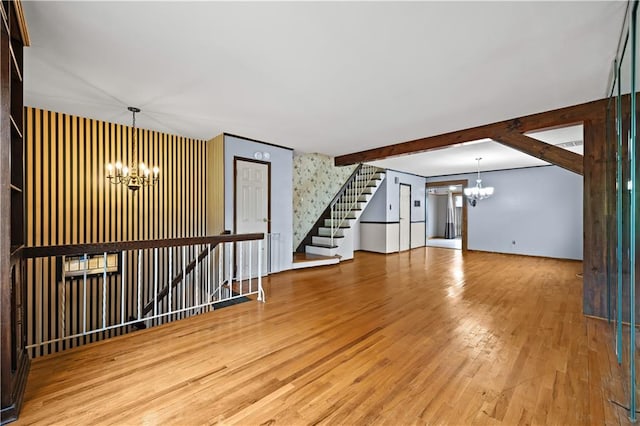 unfurnished living room with a chandelier, wood finished floors, stairs, and beam ceiling