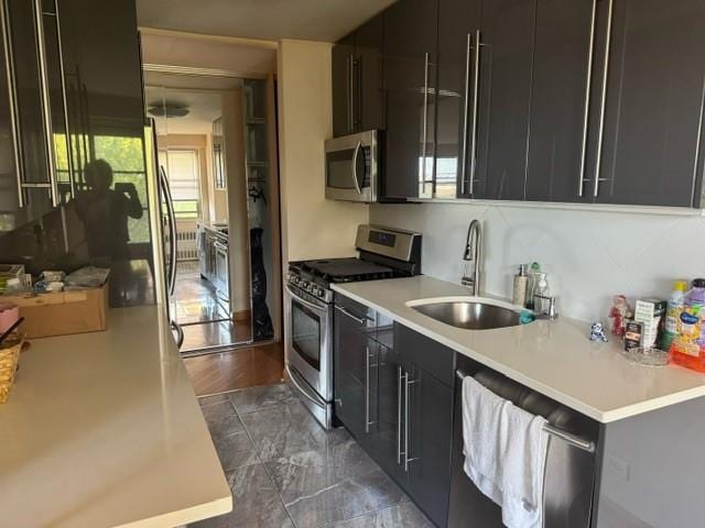 kitchen with appliances with stainless steel finishes, a sink, dark cabinetry, and light countertops