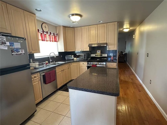 kitchen with appliances with stainless steel finishes, under cabinet range hood, a sink, tasteful backsplash, and dark countertops