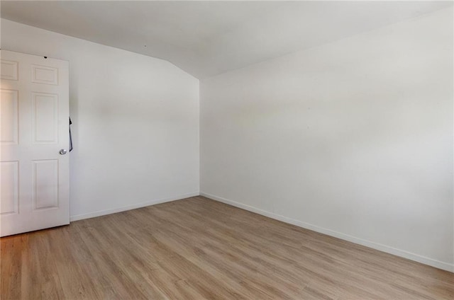 unfurnished room with light wood-type flooring, vaulted ceiling, and baseboards