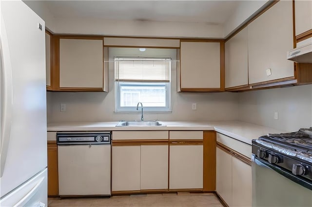 kitchen featuring freestanding refrigerator, dishwashing machine, a sink, range with gas stovetop, and light countertops