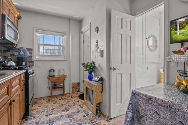 1505 E 54th St, Brooklyn, NY 11234 - kitchen with stainless steel microwave, black gas range oven, brown cabinetry, light stone finish flooring, and backsplash