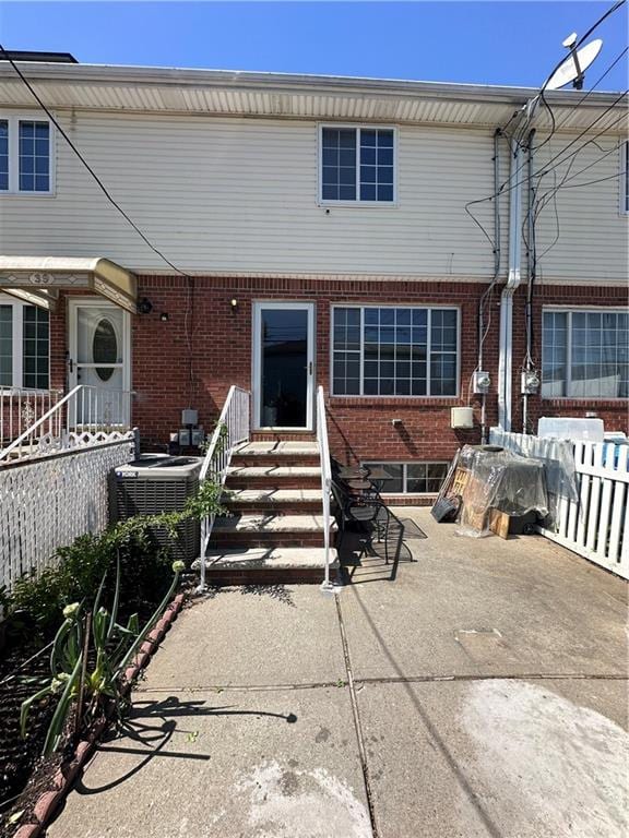 rear view of house featuring entry steps, brick siding, central AC, and a patio