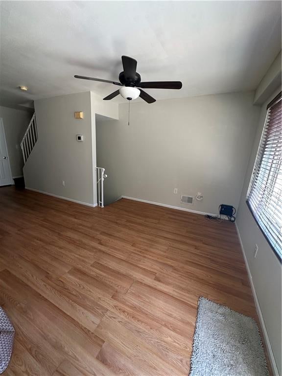 spare room with a ceiling fan, baseboards, light wood-style flooring, and stairs