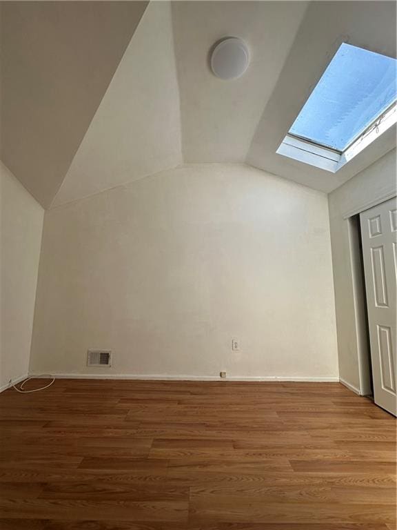 additional living space featuring vaulted ceiling, a skylight, wood finished floors, and baseboards