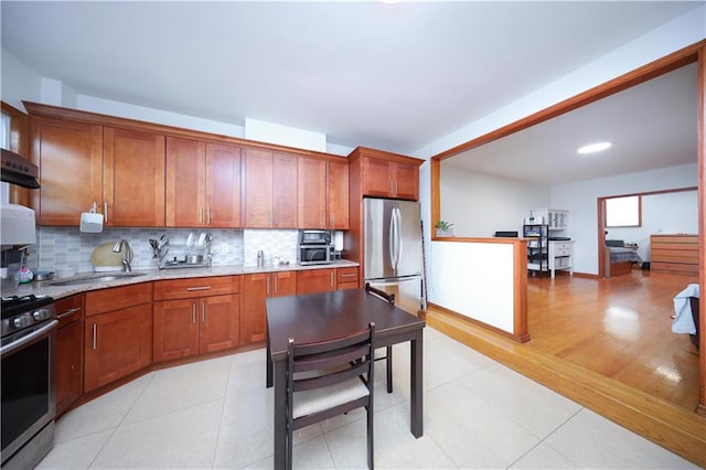 kitchen with appliances with stainless steel finishes, a sink, decorative backsplash, brown cabinetry, and range hood