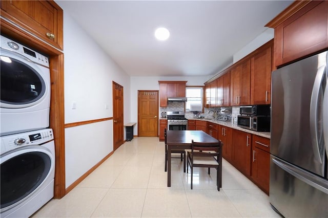 kitchen featuring stainless steel appliances, stacked washer / drying machine, decorative backsplash, under cabinet range hood, and light tile patterned floors