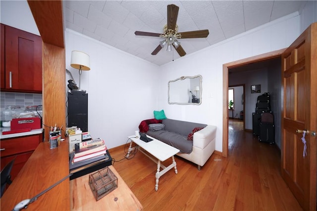 living area with wood finished floors, ceiling fan, and ornamental molding